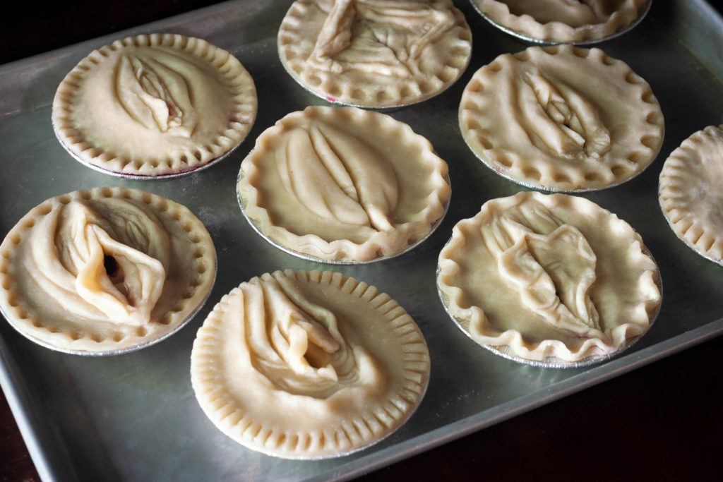 Baking pan full of unbaked pies with diverse vulva pie crust designs