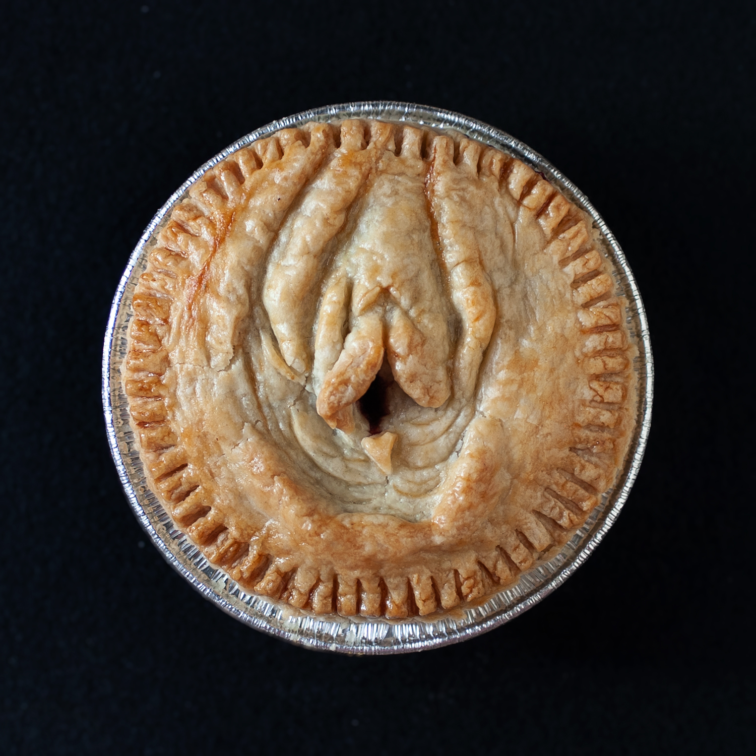 baked pie with vulva pie crust art on a black background