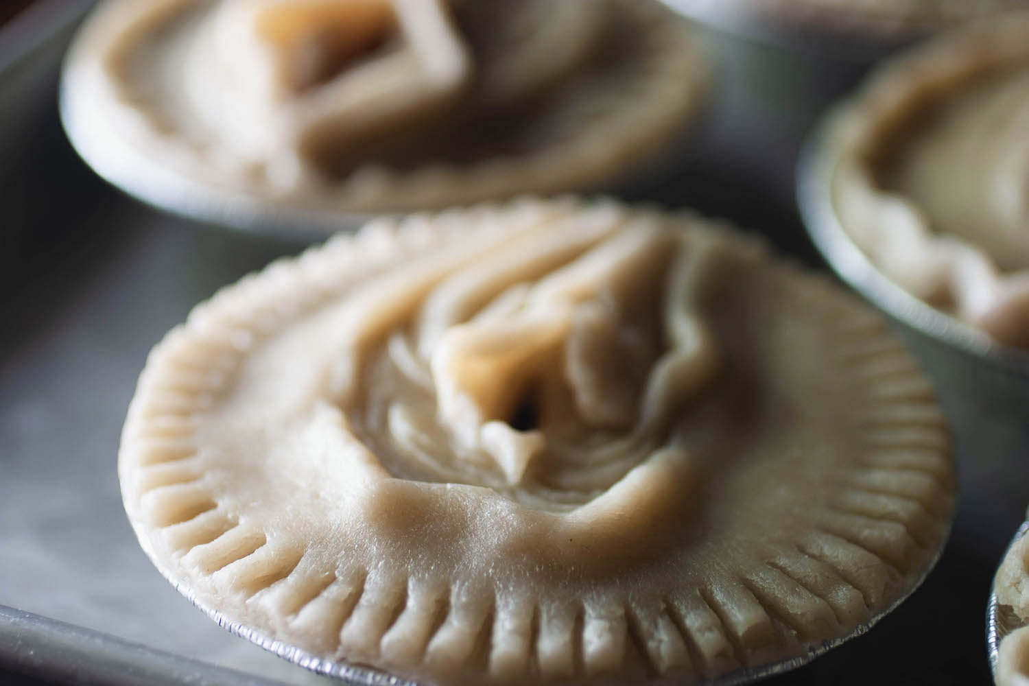 A view of a pie crust sculpted to look like a vulva from a 45 degree angle, the pie is on a baking sheet with other pies