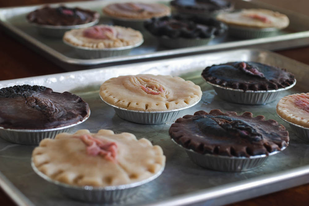 Two baking sheets filled with pies with vulva pie crust designs