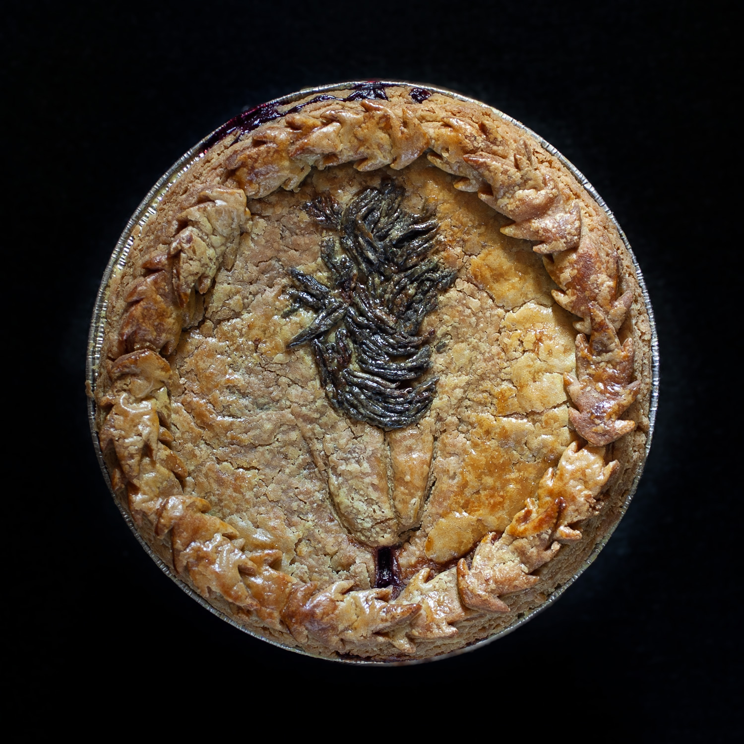 six inch baked pie with pie crust leaves around the edge and hand sculpted pie crust art that looks like a vulva with brown pubic hair