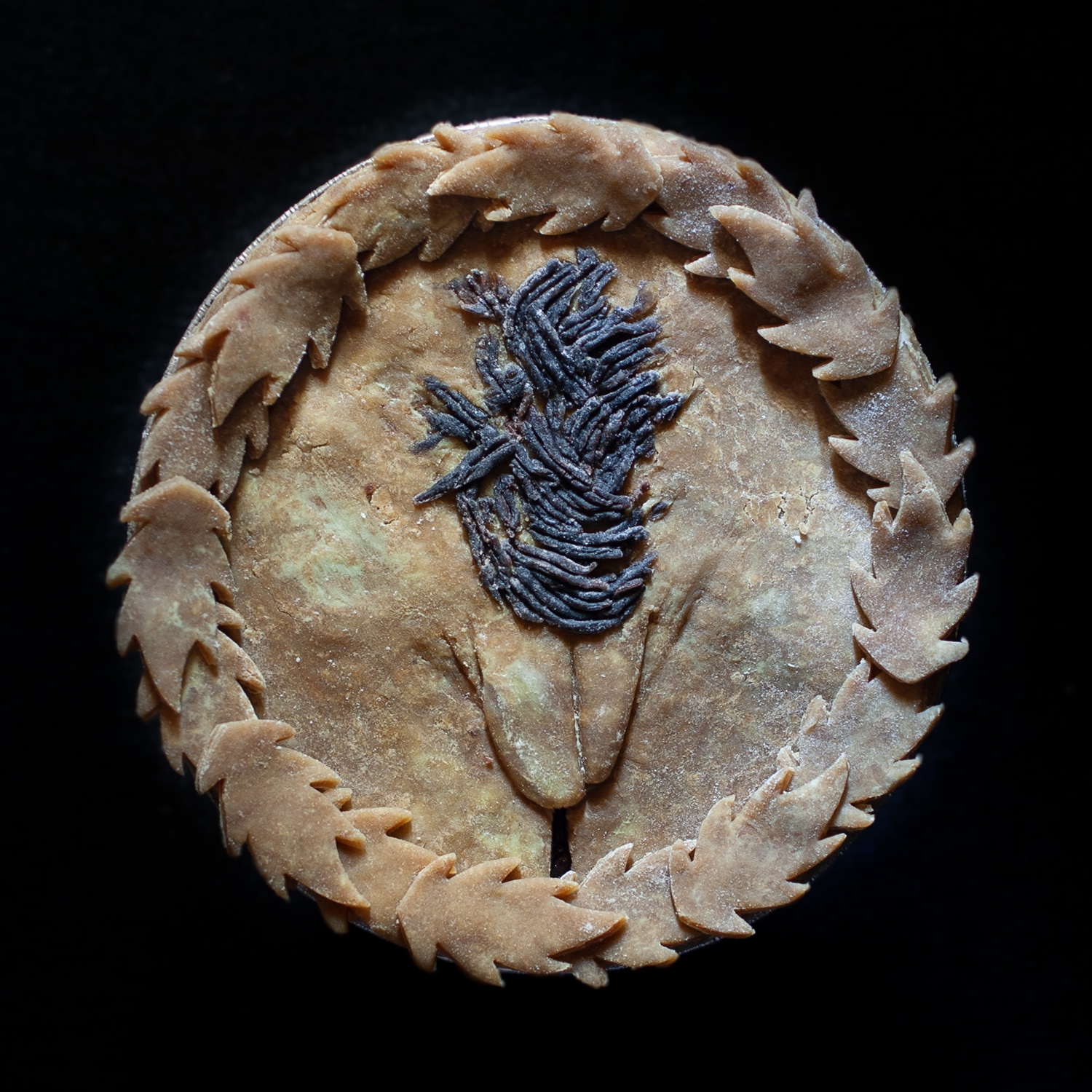 six inch unbaked pie with pie crust leaves around the edge and hand sculpted pie crust art that looks like a vulva with brown pubic hair