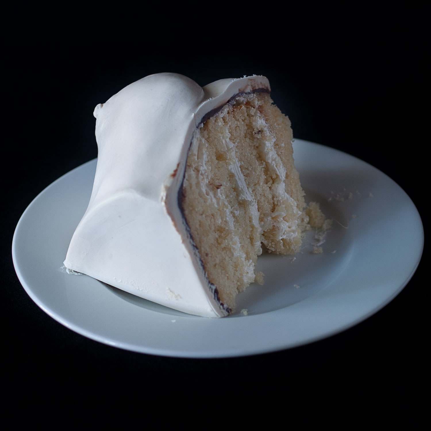 Slice of cake on small white plate. The cake is hand sculpted cake with a breast made of modeling chocolate.