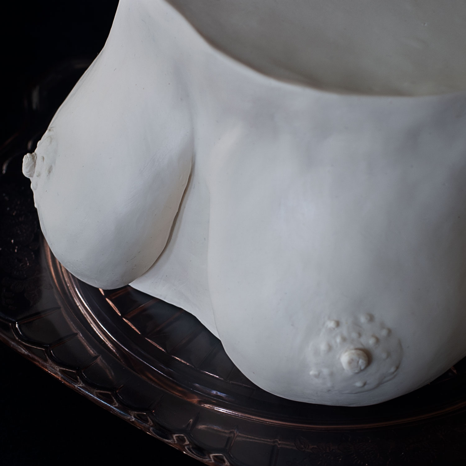 A top-down view of a very realistic boob cake sitting on a pink depression glass cake plate 