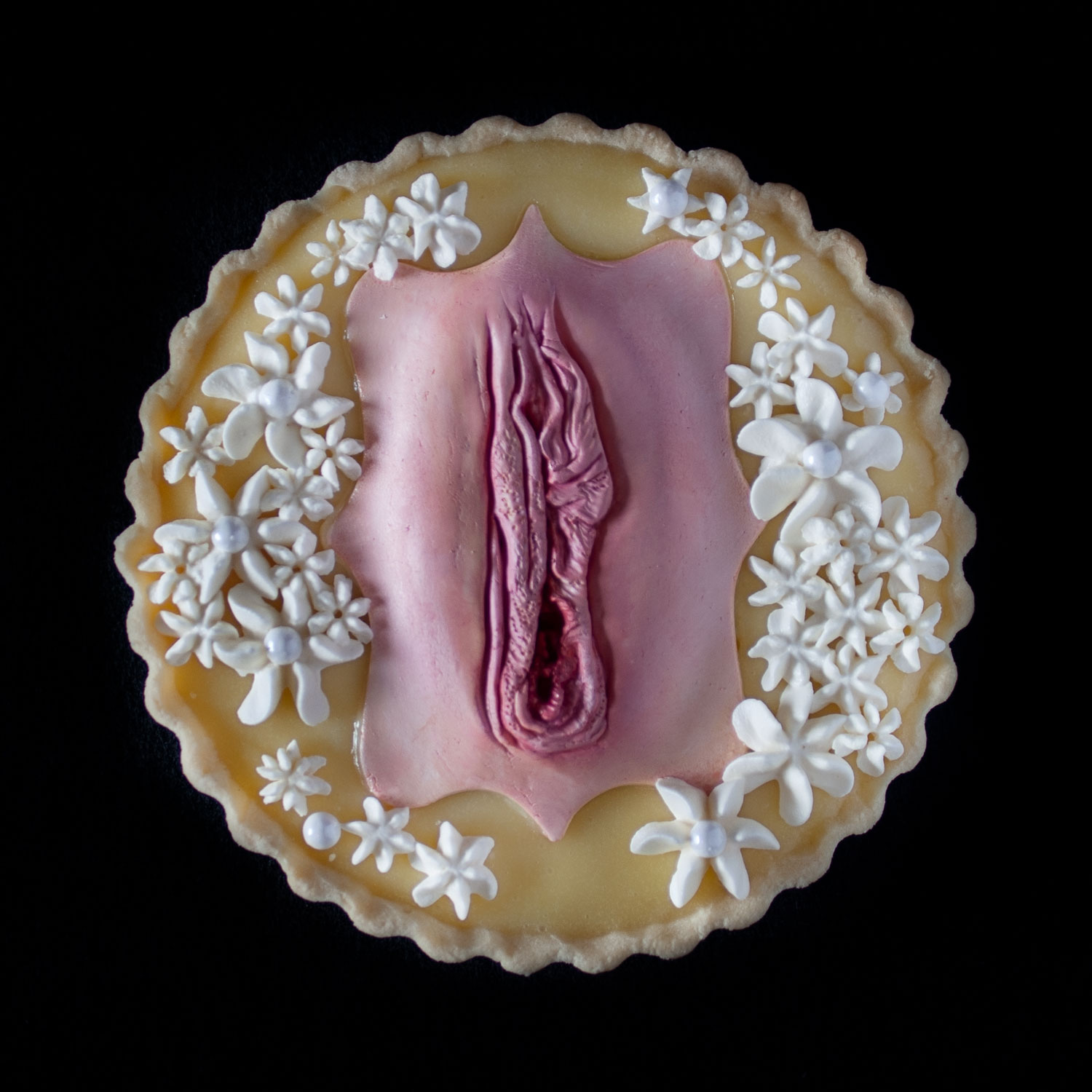 A lemon cream tart with a hand sculpted vulva decorating the top. The vulva is painted to look like real flesh.