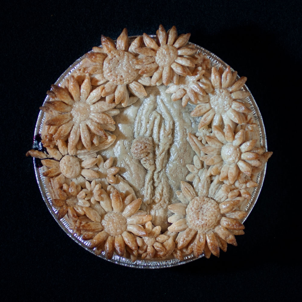 Baked blueberry pie with pie crust art. A wreath of sunflowers surrounds a realistic human vulva. 