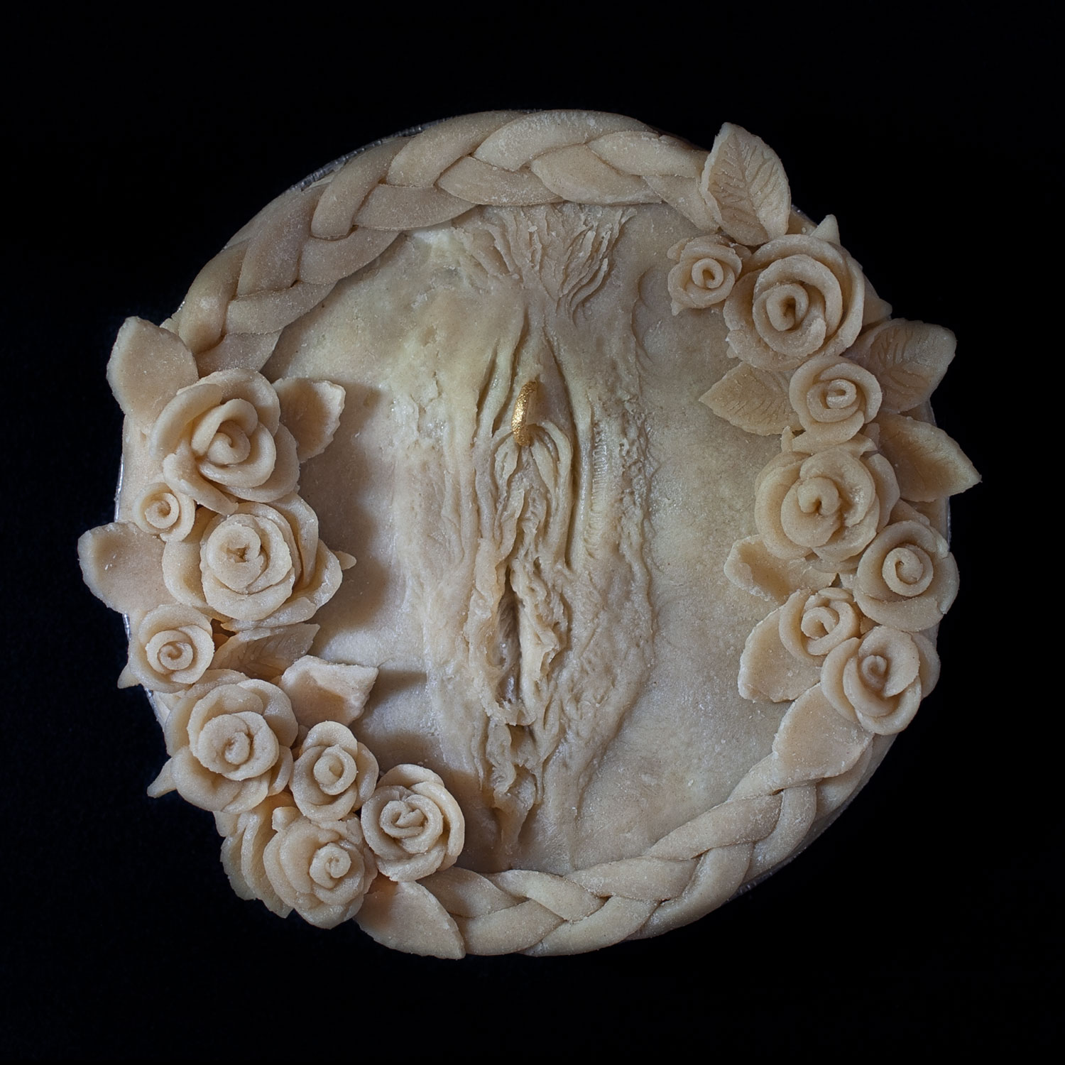 Unbaked six inch pie with pie crust art vulva with a golden ring piercing and roses surrounding it. 
