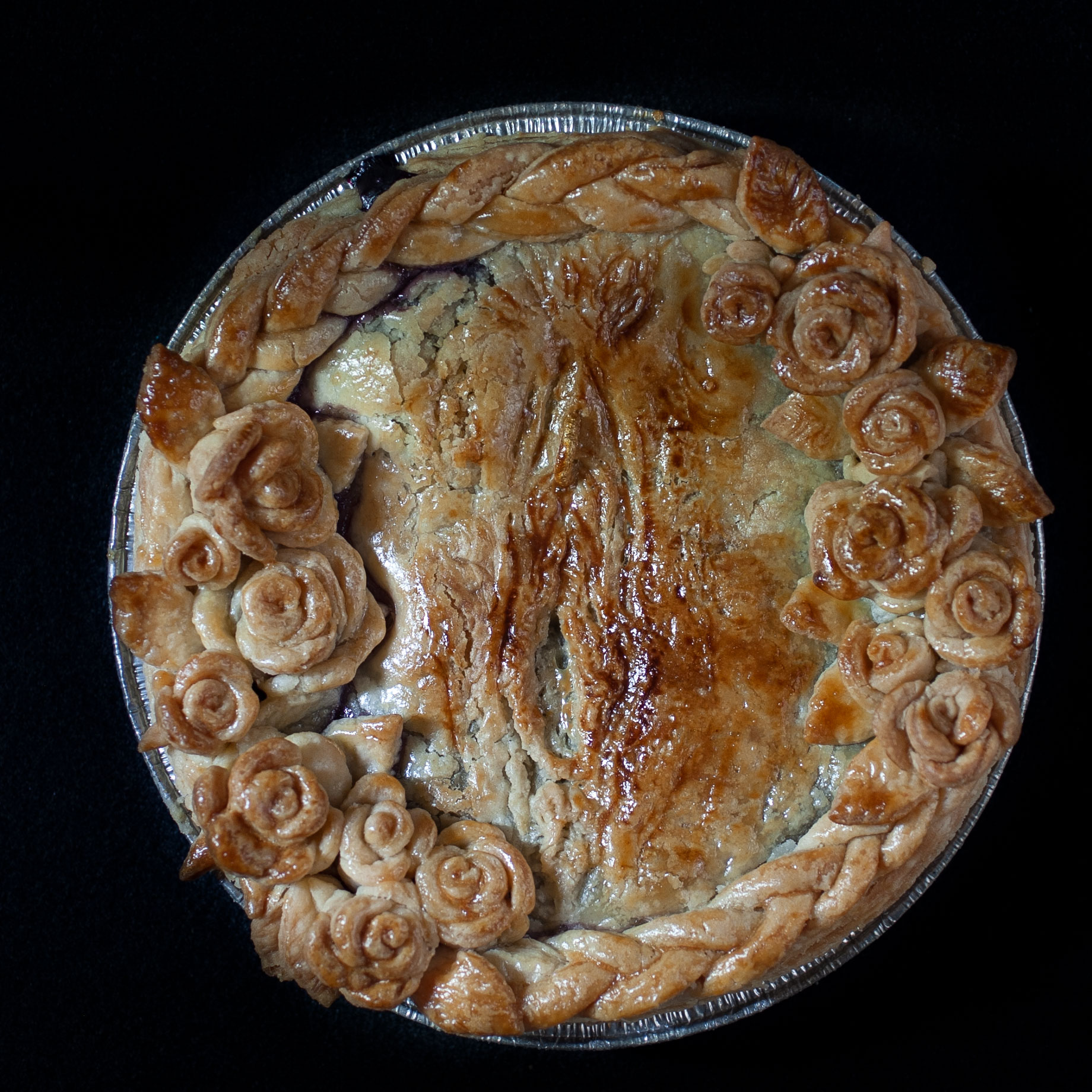 Baked six inch blueberry pie with pie crust art vulva with a golden ring piercing and roses surrounding it. 