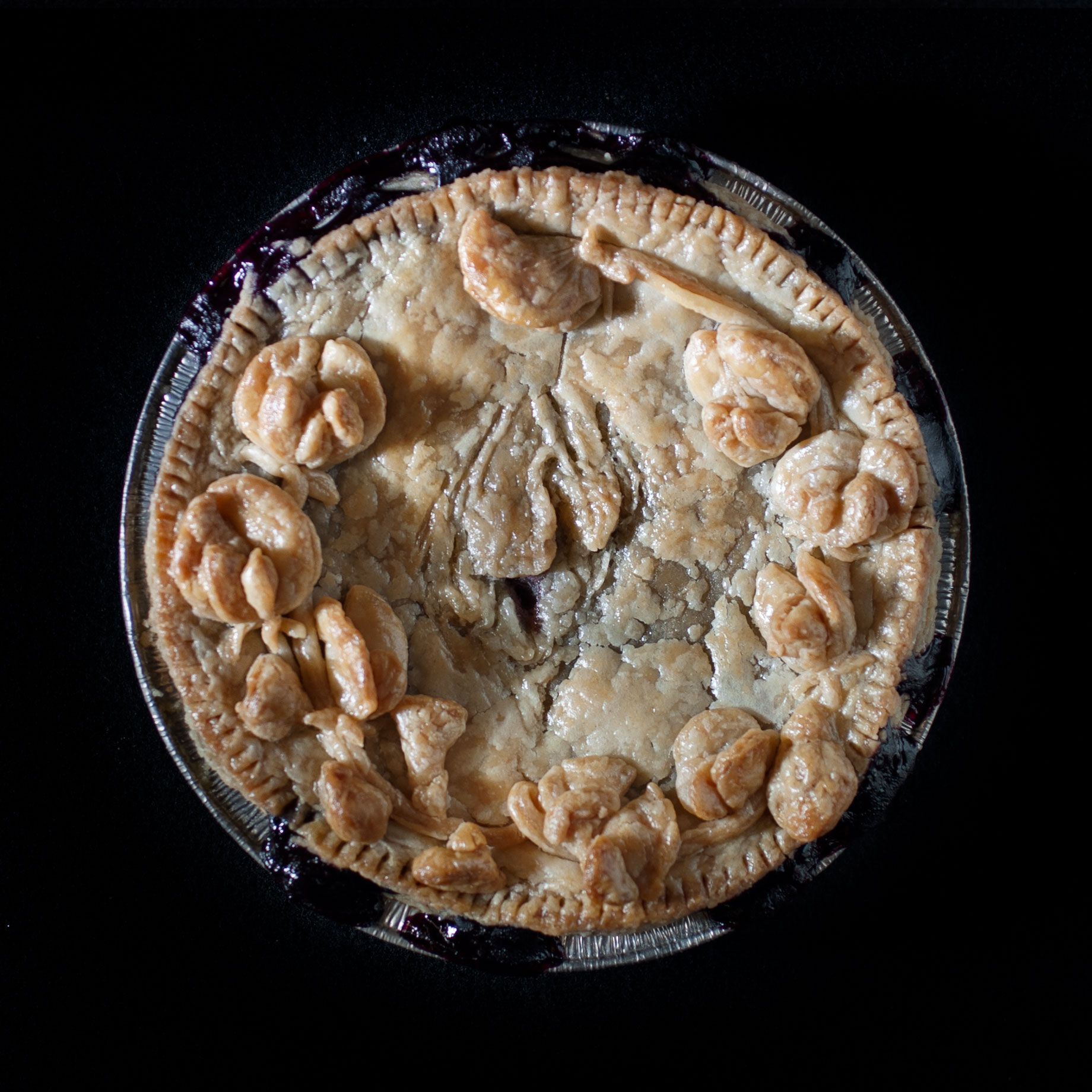 Baked pie with hand sculpted pie crust art. The pie features vulva art in the center surrounded by sculpted sweet pea flowers.