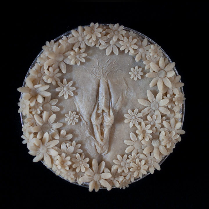 Unbaked pie with hand sculpted pie crust art. Pie crust daisies surround a realist vulva made of pie crust.