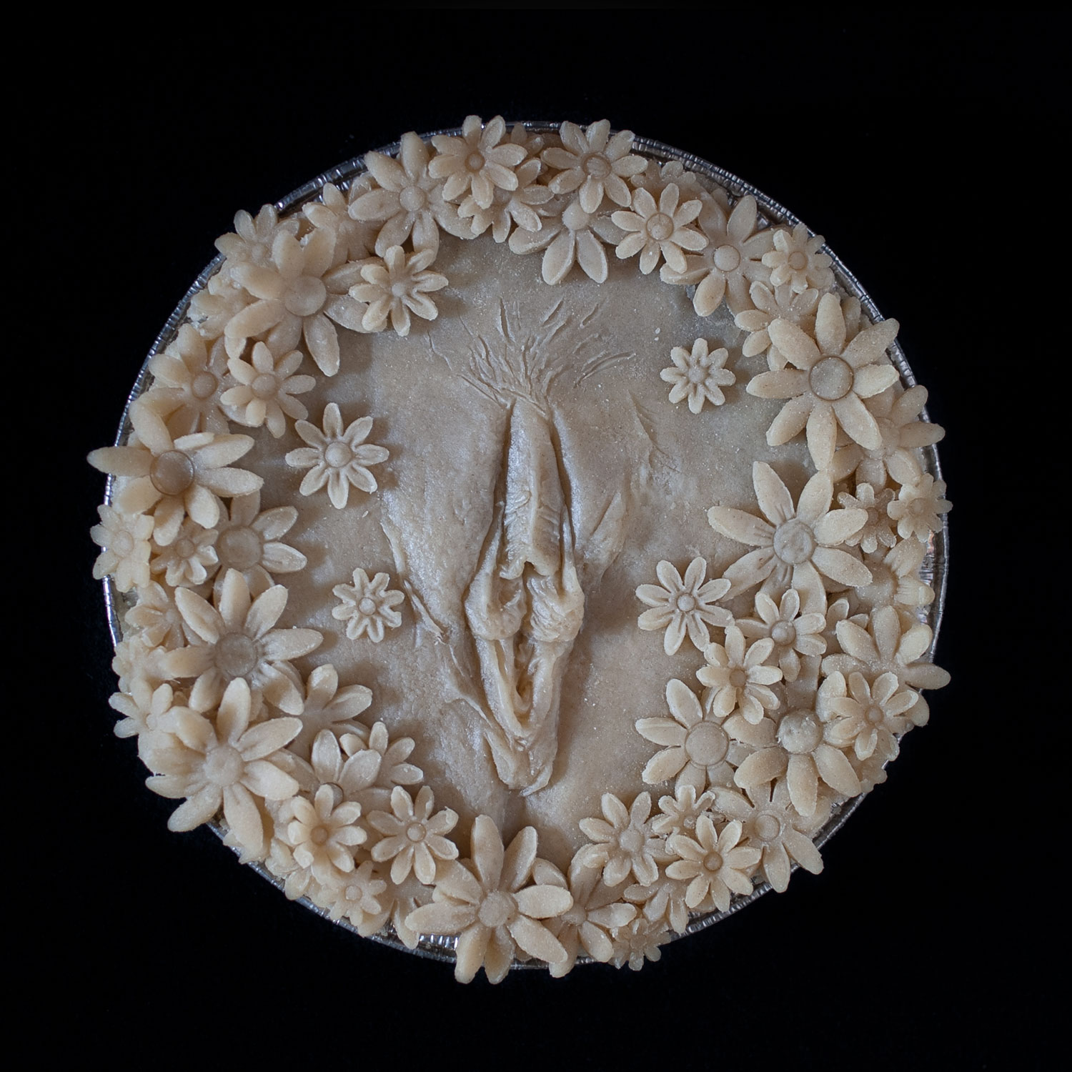 Unbaked pie with hand sculpted pie crust art. Pie crust daisies surround a realist vulva made of pie crust. 