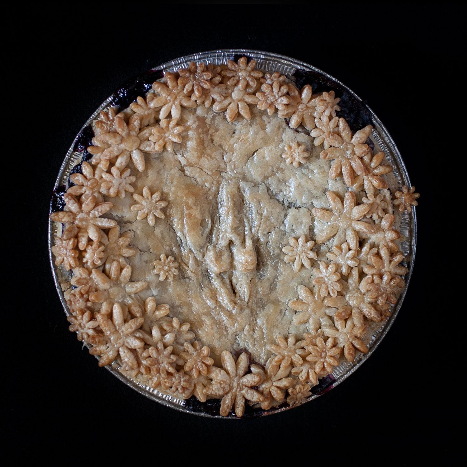 Baked pie with hand sculpted pie crust art. Pie crust daisies surround a realist vulva made of pie crust. 