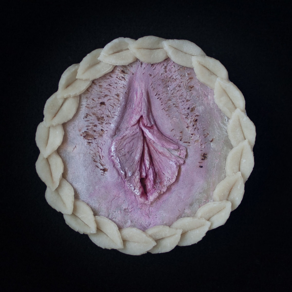 Vulva pie on black background. Pie is a realistic vulva made of pie dough painted with edible paints.