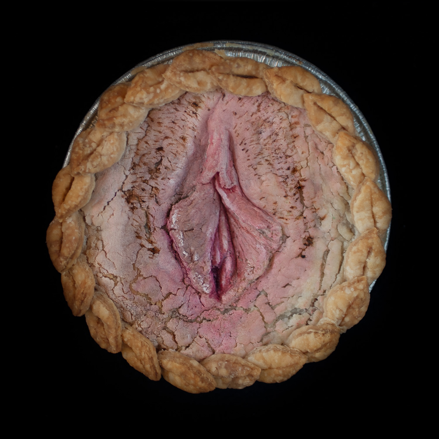 Mini vulva pie on black background with hand sculpted, hand painted vulva art surrounded with pie crust leaves