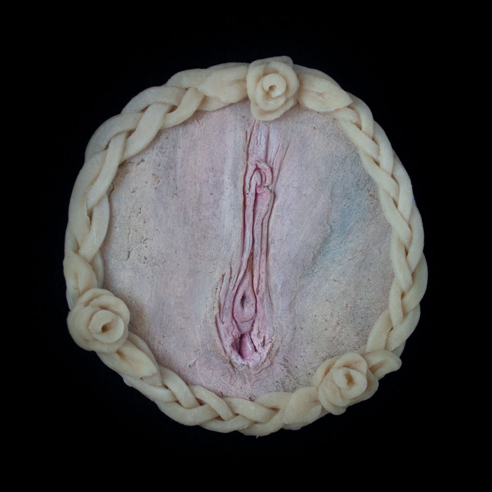 A pie with vulva pie crust art on a black background.