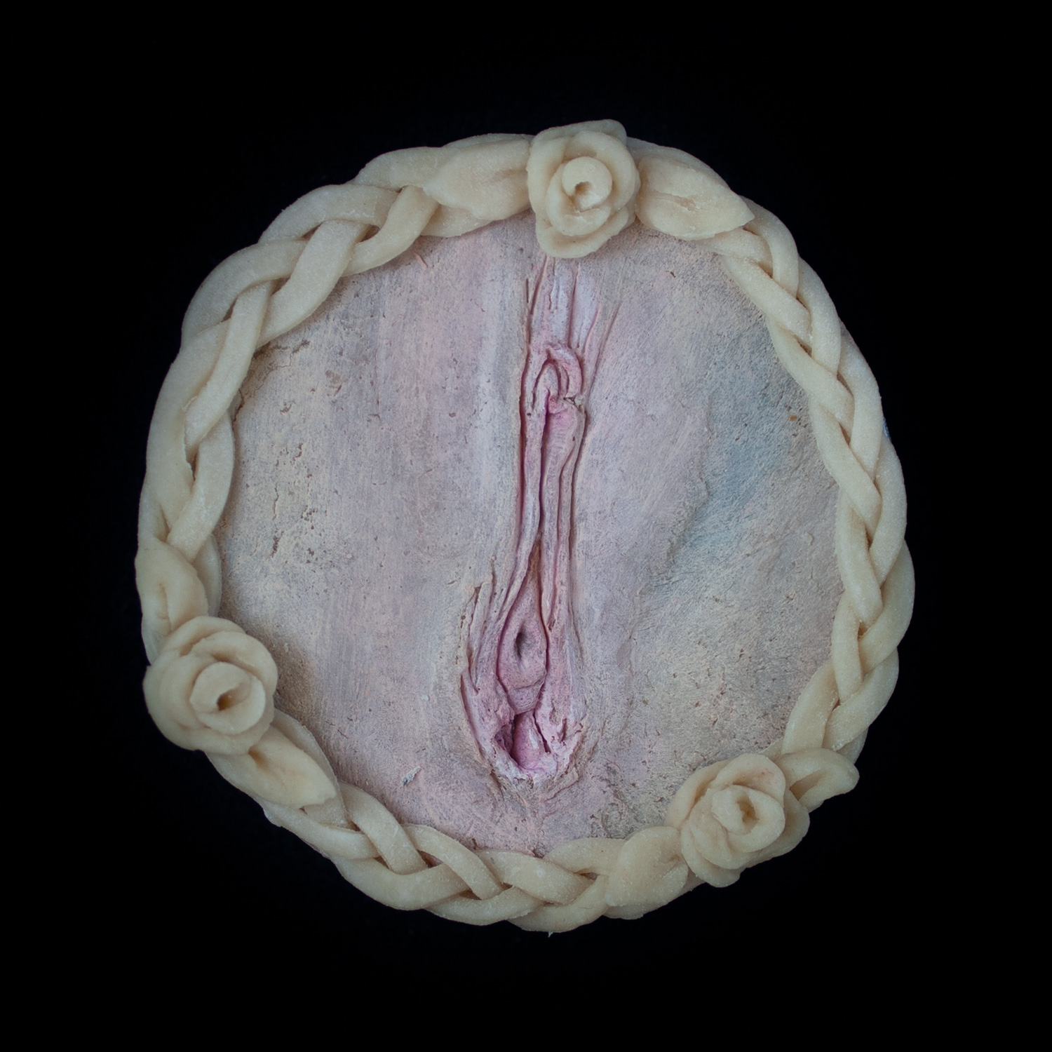 A pie with vulva pie crust art on a black background. 