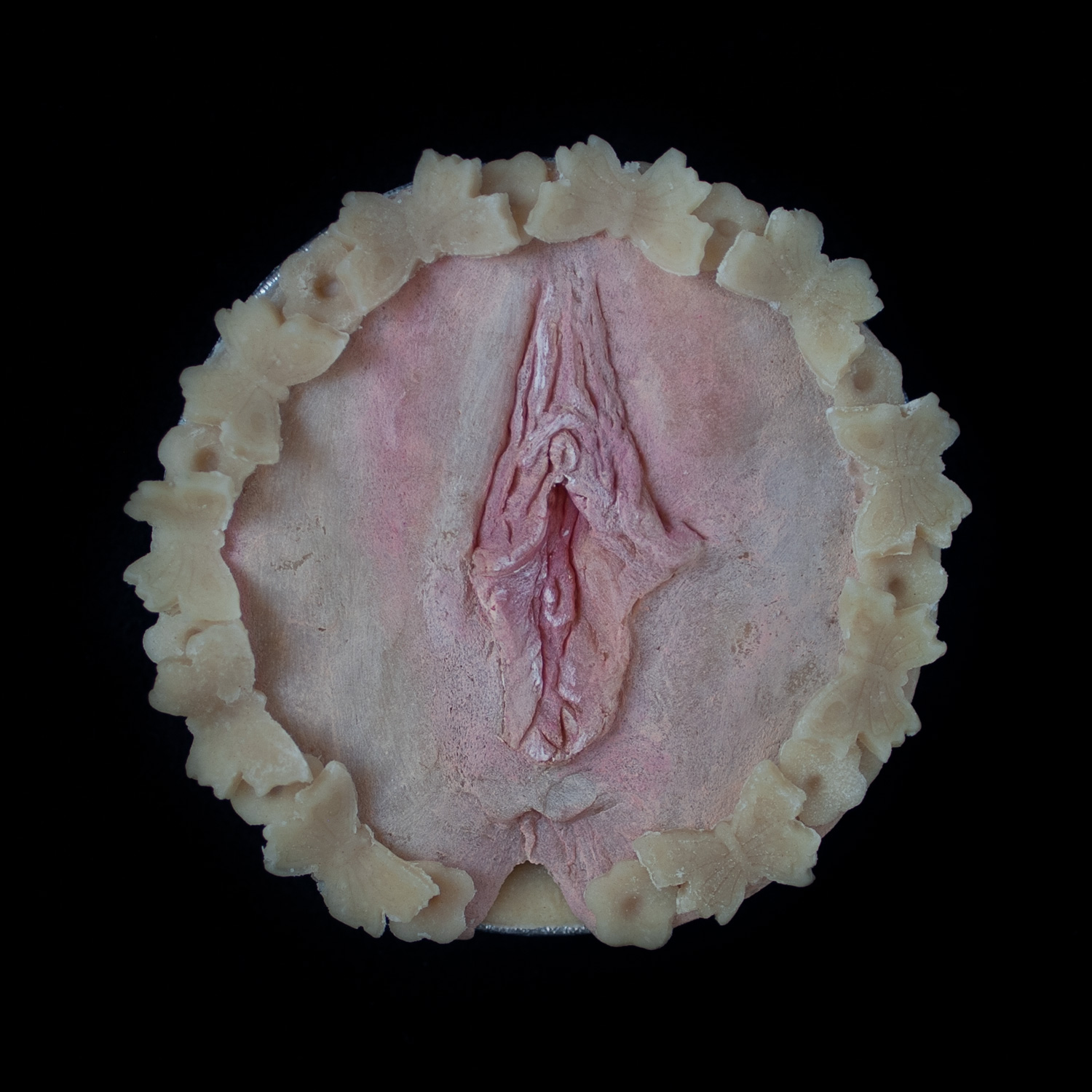 A pie on a black border with hand sculpted vulva made of pie dough. 