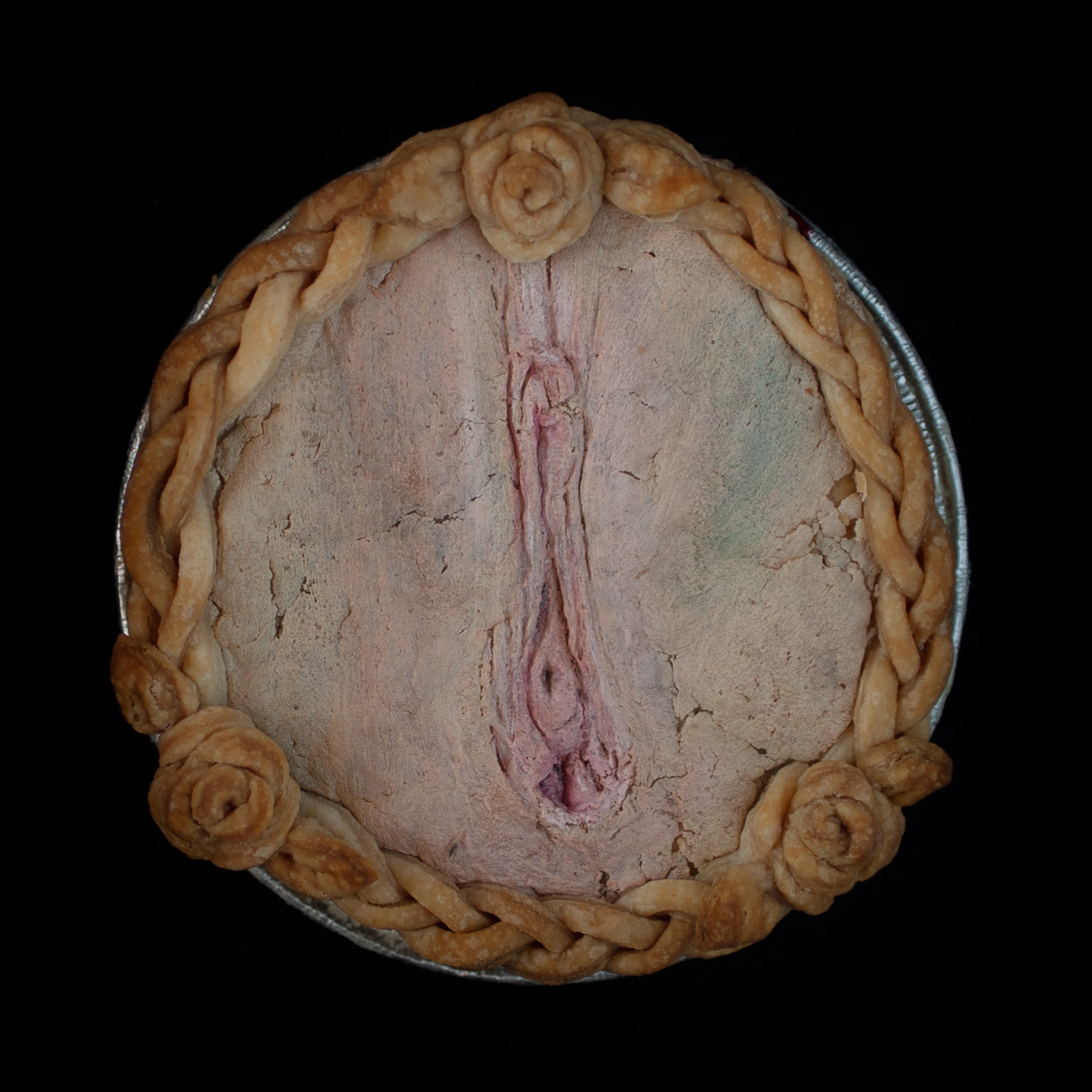 A baked pie with vulva pie crust art on a black background. 