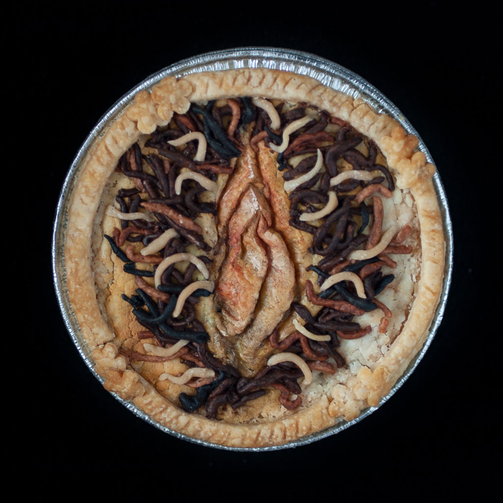 Baked Pie on black background with realistic vulva art made from multicolored pie dough. 