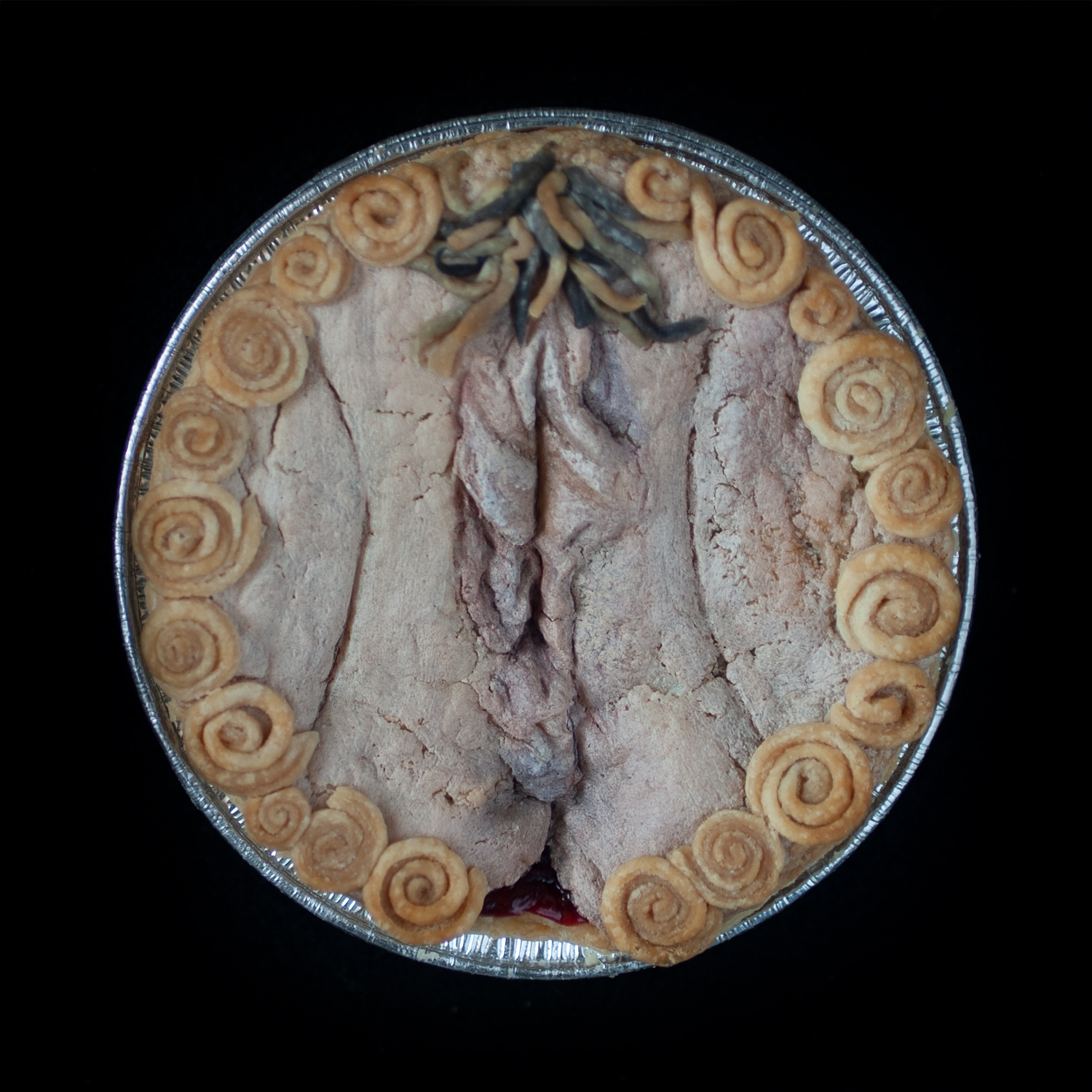 Mini-pie on a black background decorated with hand sculpted, hand painted vulva art surrounded with spiral border