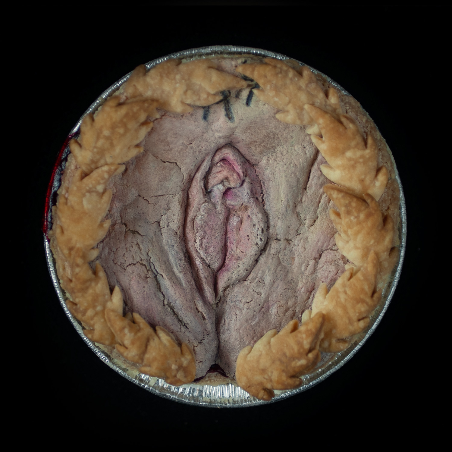 A baked vulva pie on a black background. The pie is surrounded with pie crust leaves and is painted to look like a realistic vulva. 