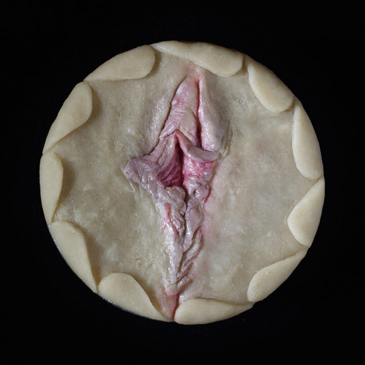 Unbaked pie on a black background. The pie art is made to look like a human vulva.