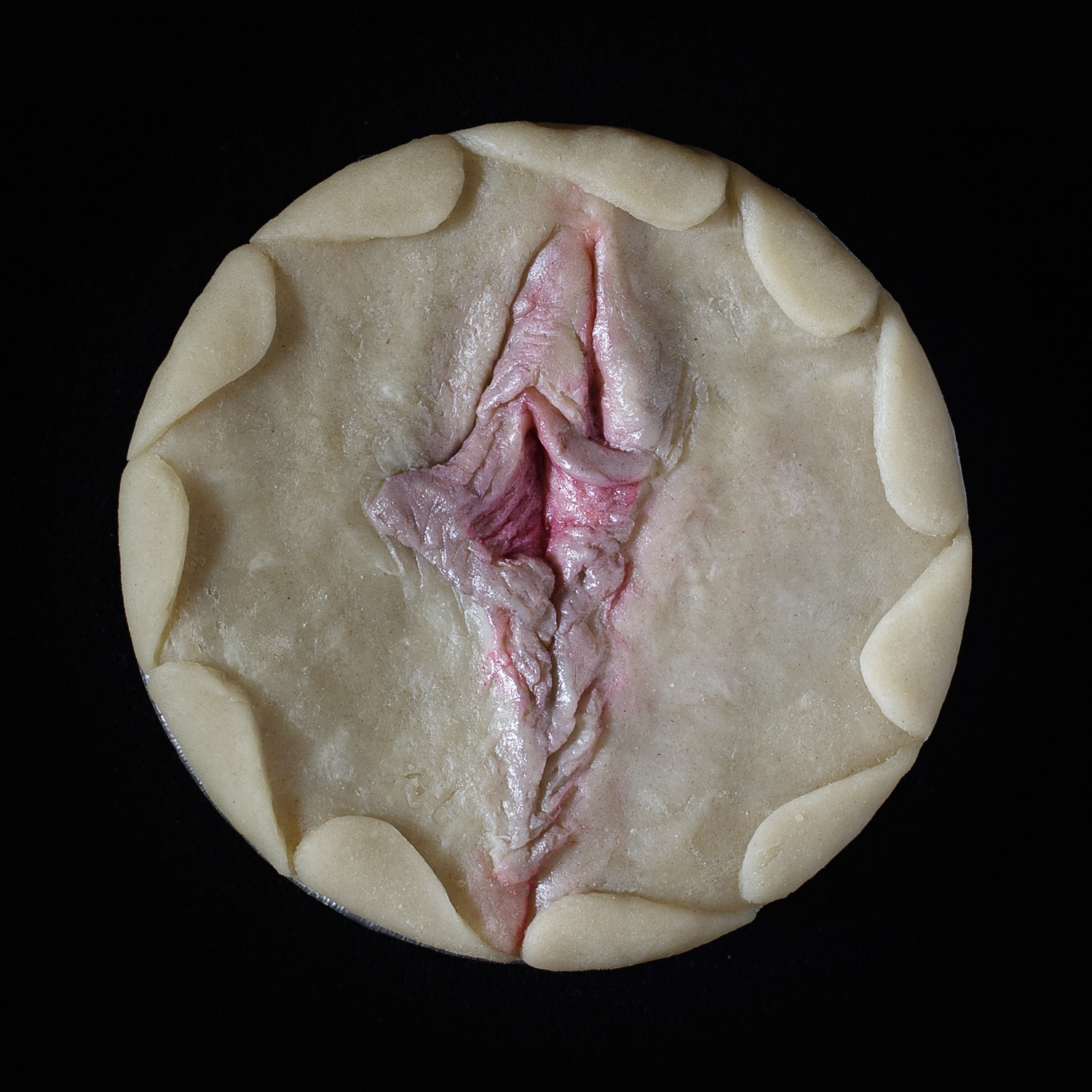 Unbaked pie on a black background. The pie art is made to look like a realist human vulva.