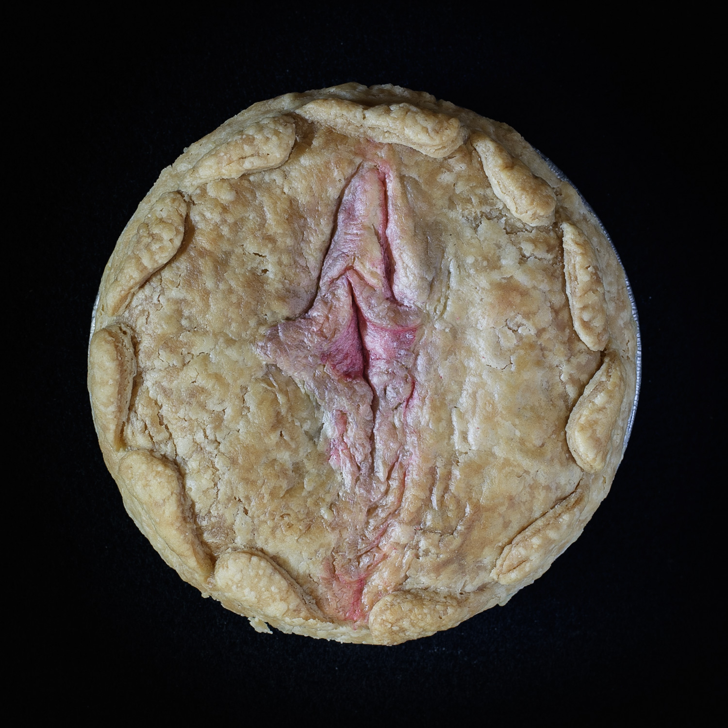 Baked pie on a black background. The pie art is made to look like a realist human vulva.