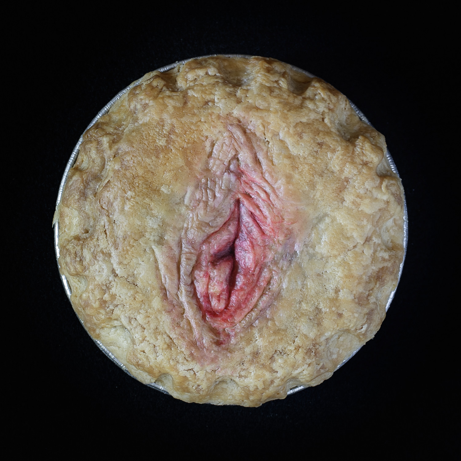 Baked vulva pie on a black background. The pie art features a realistic vulva painted with edible paint.