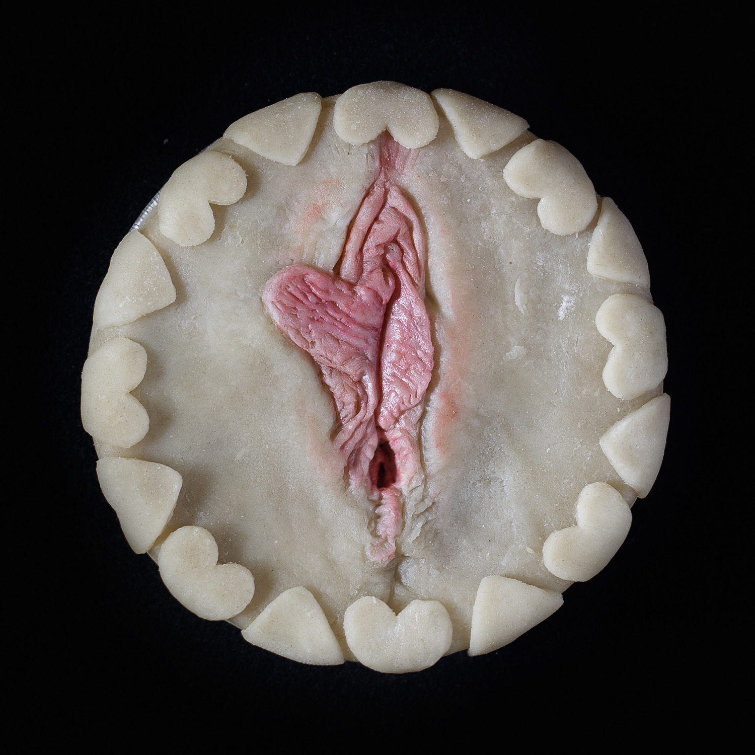 Unbaked pie decorated with hand-sculpted vulva art on a black background 