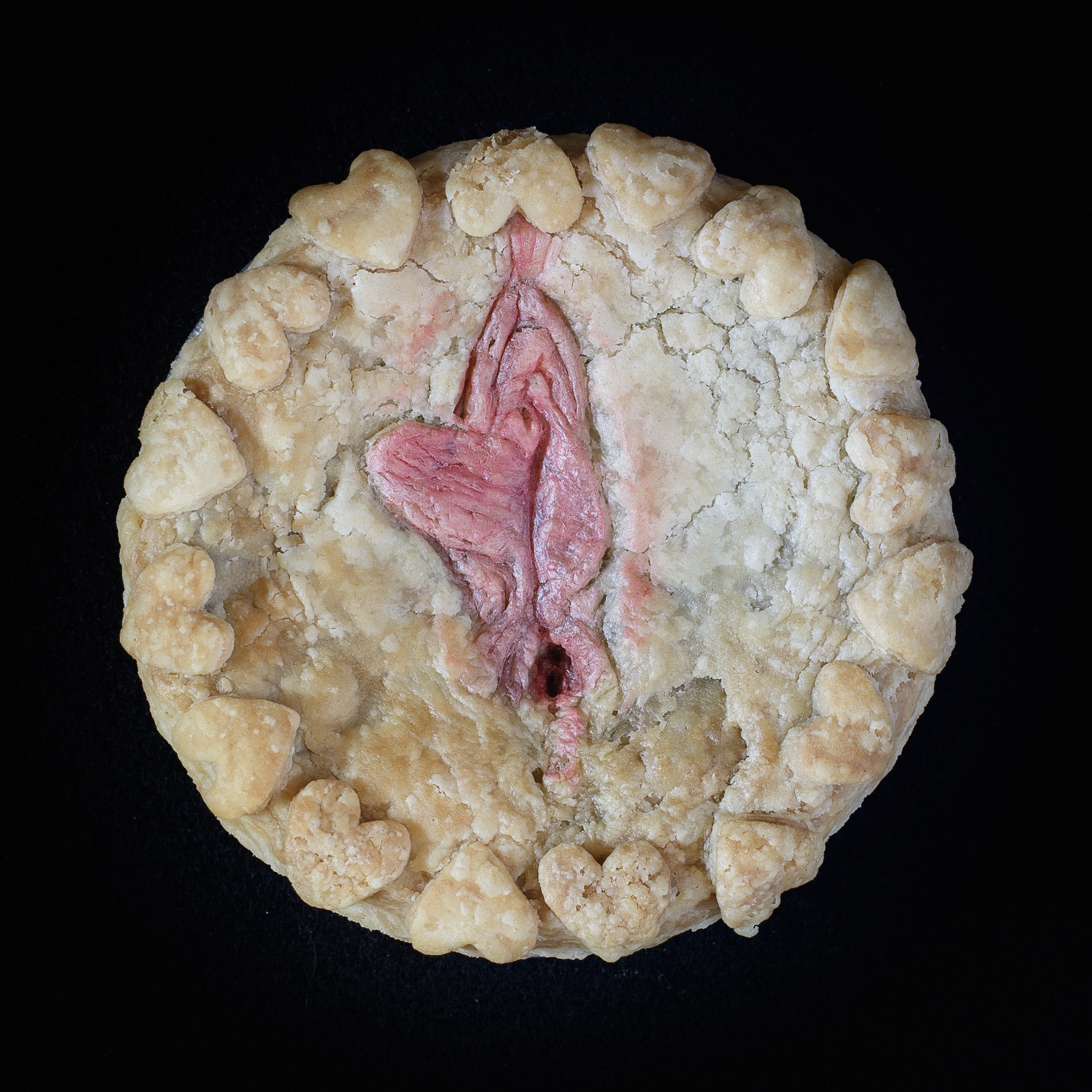 Baked pie decorated with hand-sculpted vulva art on a black background 