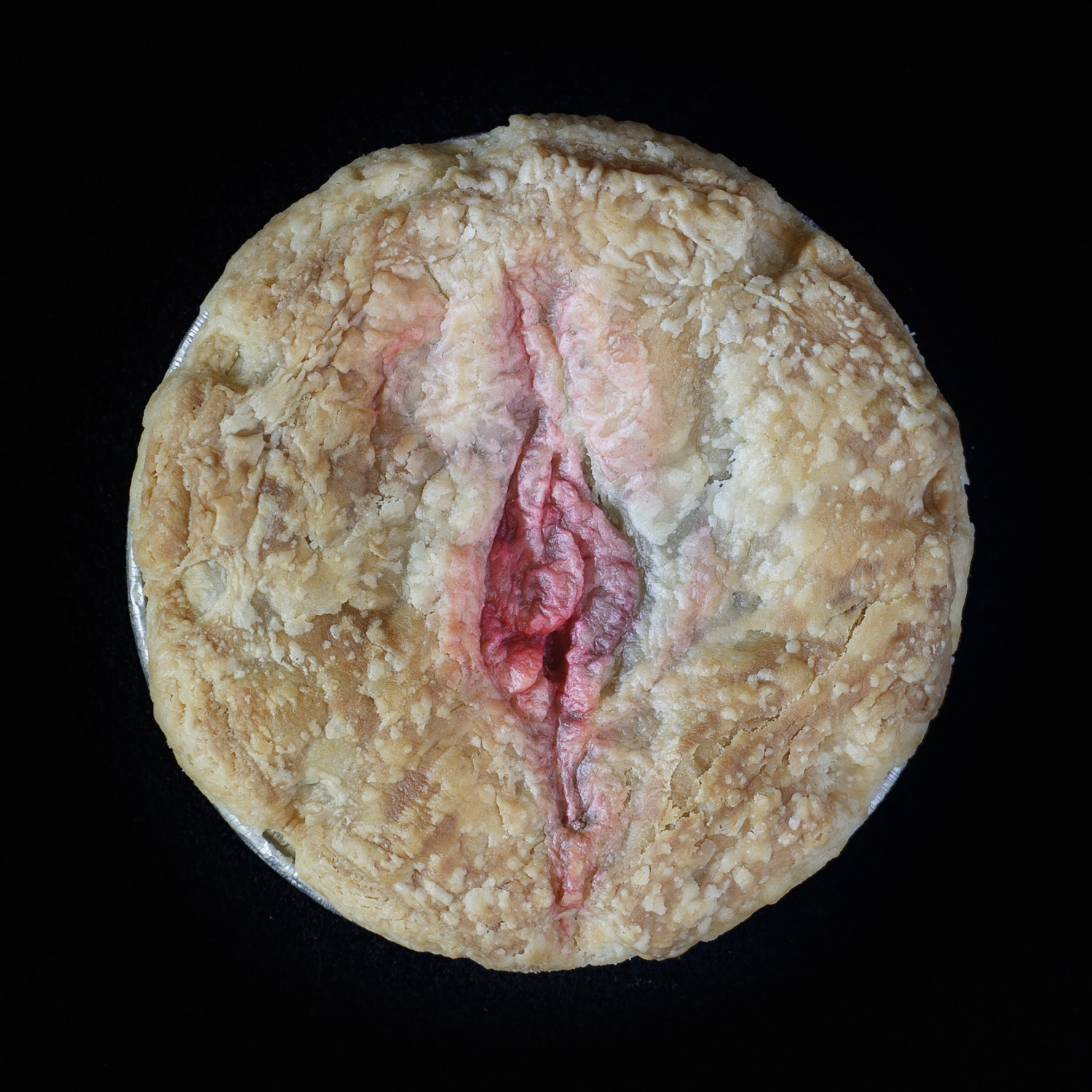 Baked Pie on a black background. The pie art depics a pink vulva