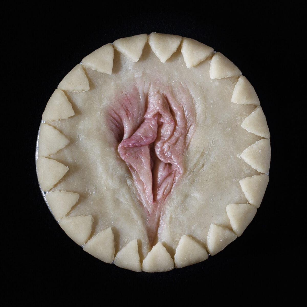 Unbaked cherry pie on a black background. The pie has hand painted vulva art made of real pie dough.