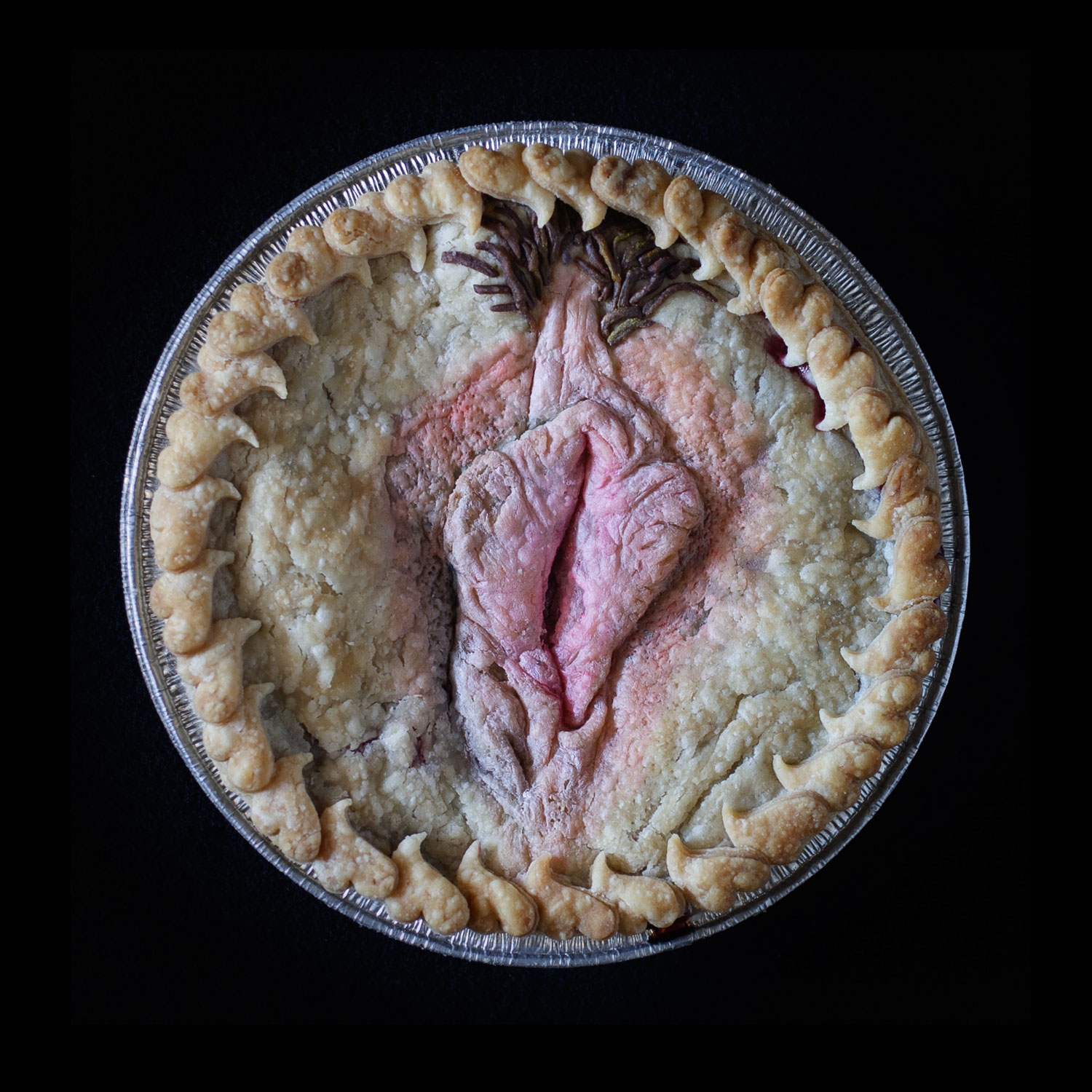 A baked pie on a black background. The pie is adorned with a realistic vulva surrounded my hearts cut out of pie dough. 