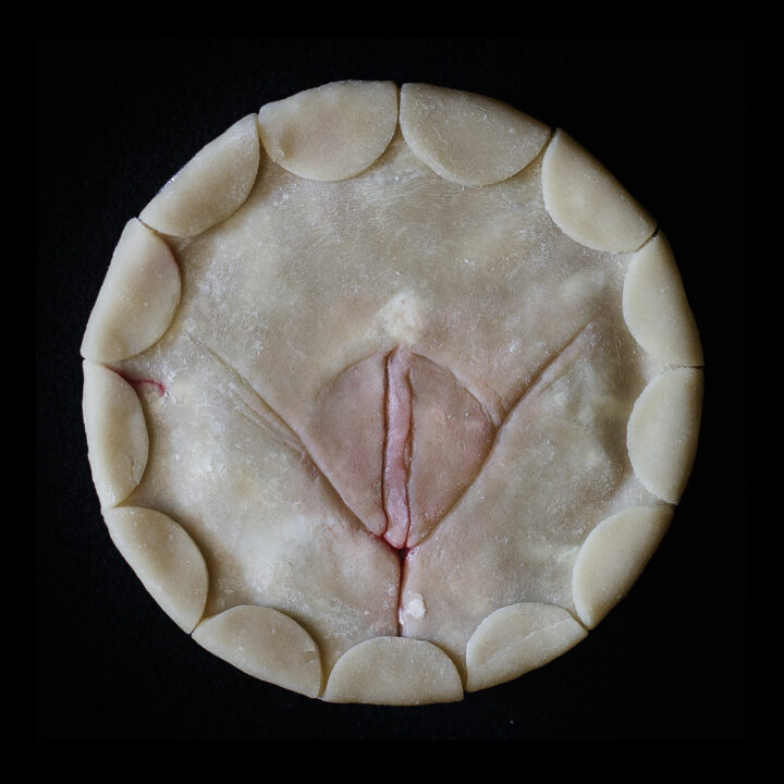 Unbaked pussy art pie on a black background. Pie has half circles around the border.