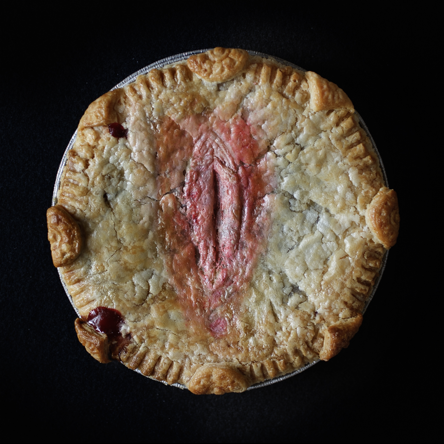 Baked pie with hand sculpted art on a black background. The pie art looks like a realistic vulva.