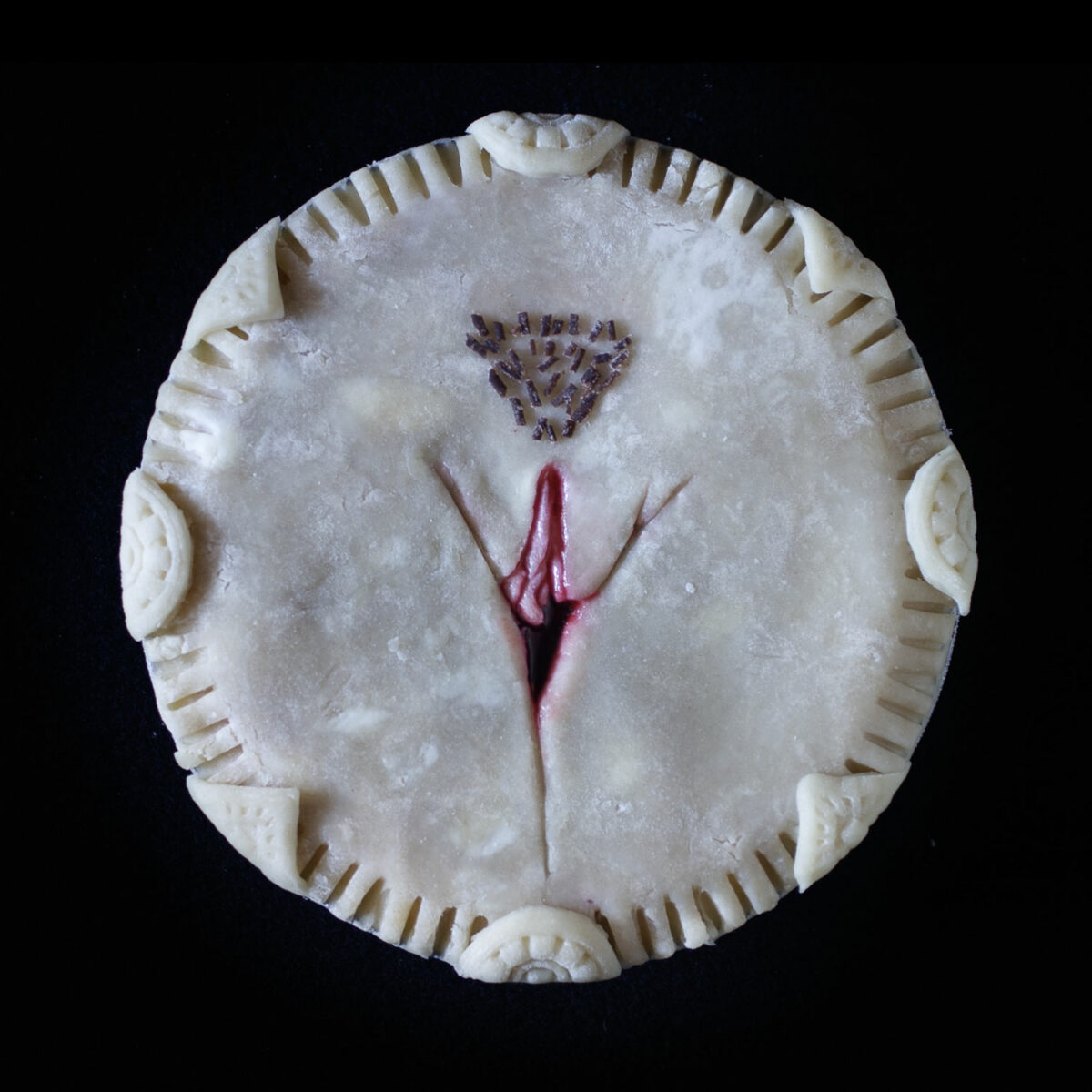 Unbaked art pie with cherry filling. The pie is sculpted to look like the frontal view of a vulva.