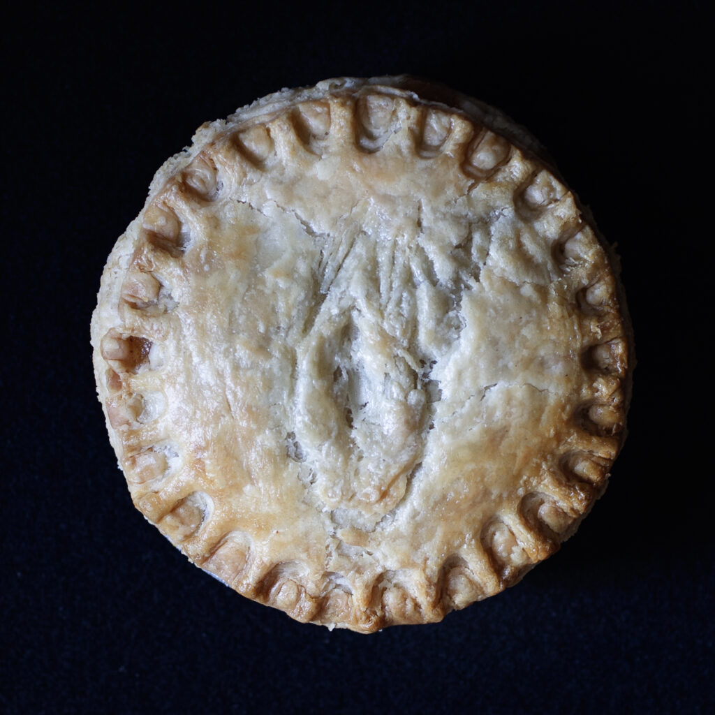 Made from scratch baked vulva pie on black background. 