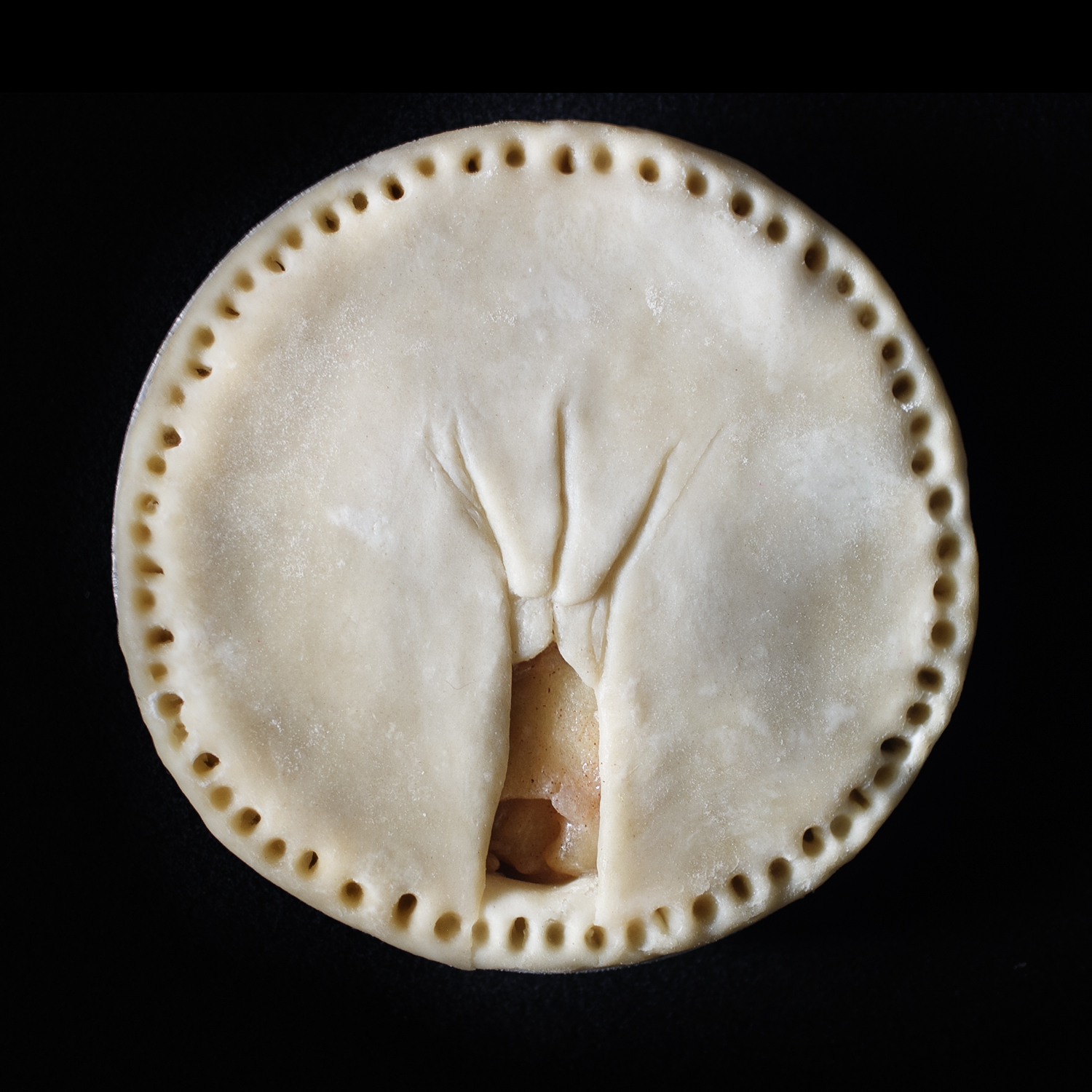 Unbaked pie on black background. The pie features a vulva sculpted out of pie dough. 