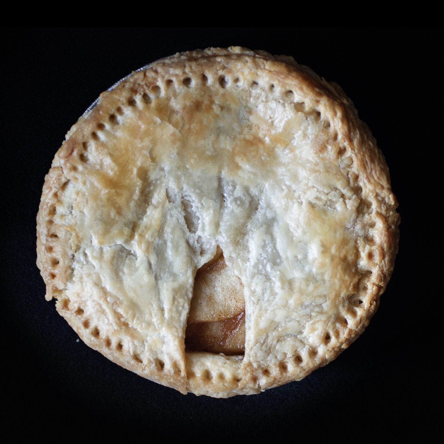 Baked pie on black background. The pie features a vulva sculpted out of pie dough. 