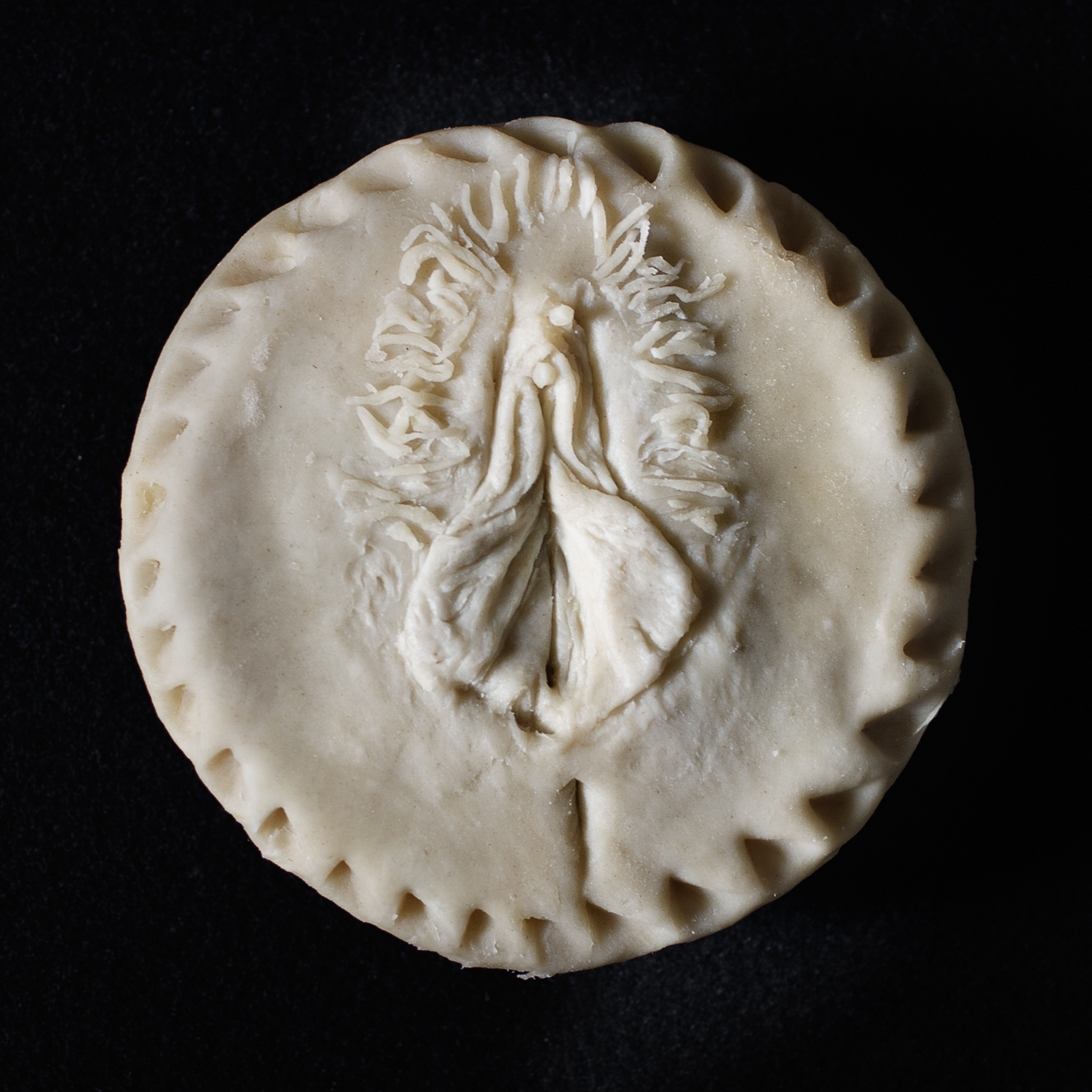 Unbaked pie featuring hand sculpted figure art, made to look like a human vulva